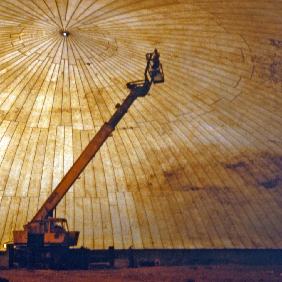 Worker inspects inflated membrane from a man basket mounted on a crane.